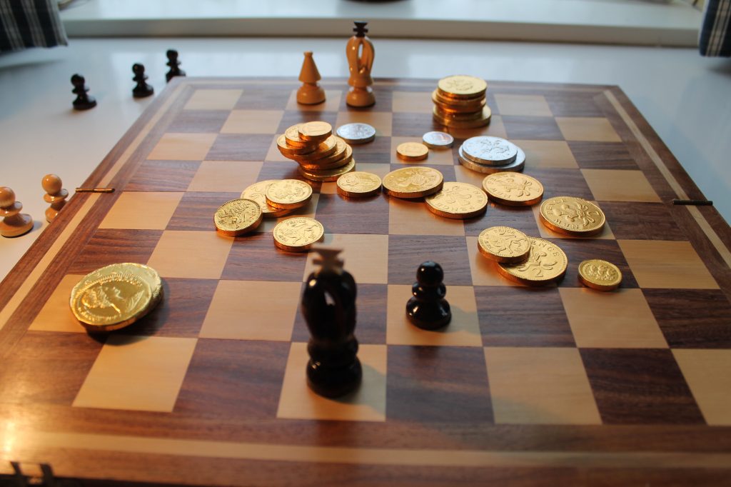 Chocolate coins and chess pieces on chessboard.